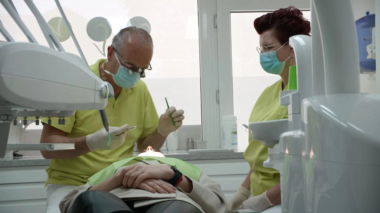 Drs. Hans van der Elst behandelt eine Patientin im Behandlungsstuhl, eine Assistentin steht daneben